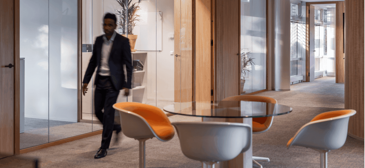 Man in suit walking past meeting rooms with glass walls