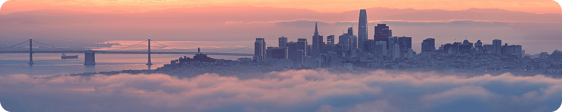 San Francisco skyline met Bay Bridge bij zonsopkomst boven de mist