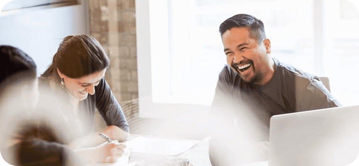 Teamleden werken samen aan tafel met laptop, glimlachend en lachend
