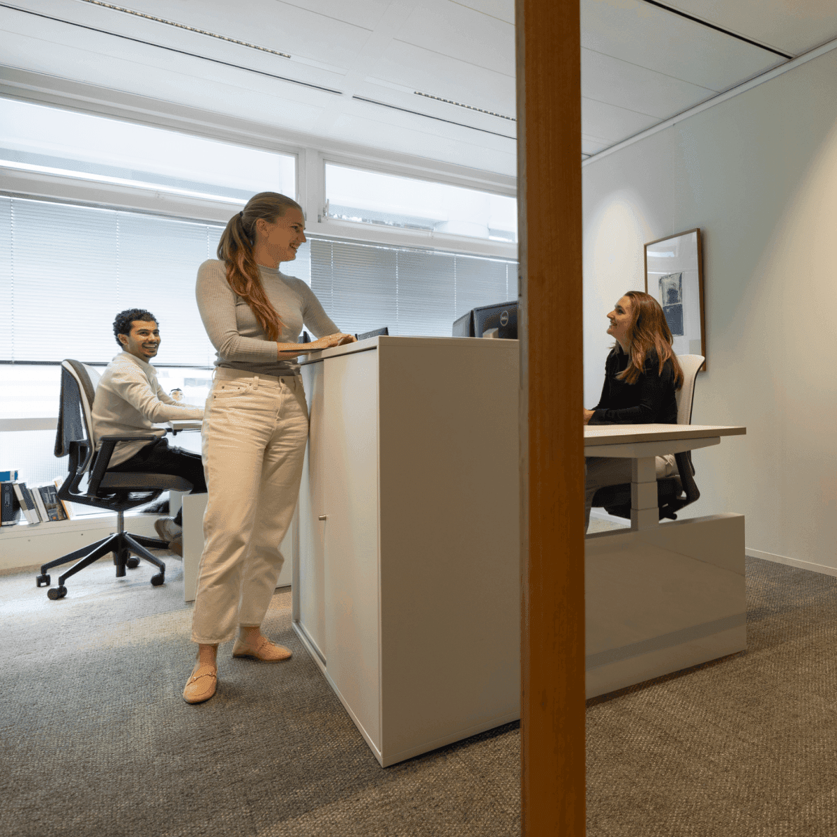 Three colleagues smiling and discussing in bright office space