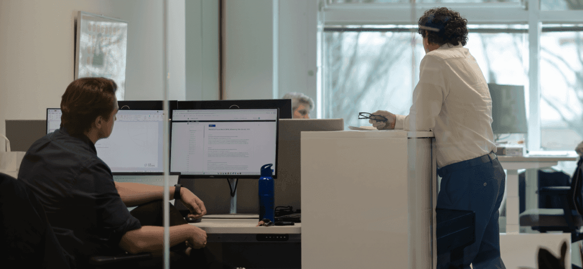 Two colleagues discussing at workstation with computer screens